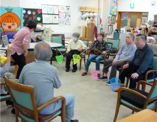 デイサービスで利用者がスタッフと一緒に輪投げのようなレクリエーションを楽しんでいる和やかな様子