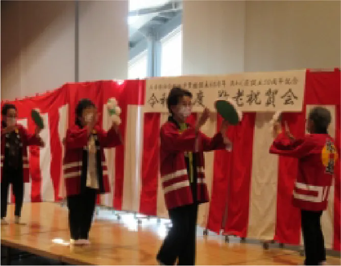 高齢者の方々が赤いはっぴを着て舞台で踊りを披露し、地域交流イベントを楽しんでいる様子