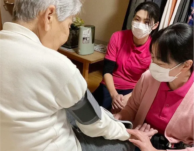 利用者の血圧を測定する訪問看護師とスタッフ
