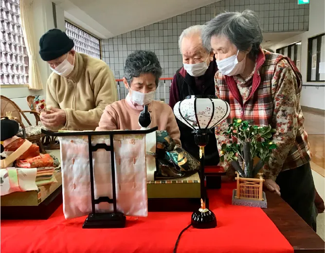 マスク姿の高齢者たちが雛人形を囲んでいる様子